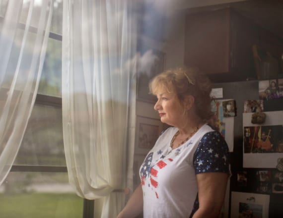 Woman in star-spangled butterfly t-shirt looks out the window of her kitchen, standing by her fridge covered with photos and fun magnets