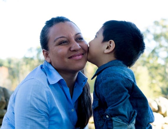 A smiling mom gets a kiss from her toddler in a park