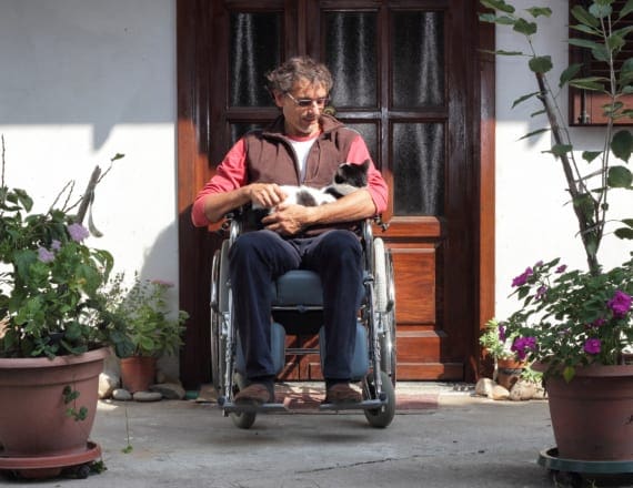 Man in wheelchair outside his front door, with a cat on his lap