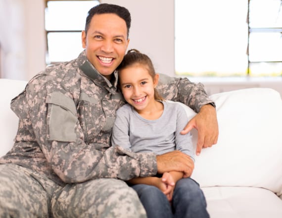 Uniformed soldier smiling on couch with daughter