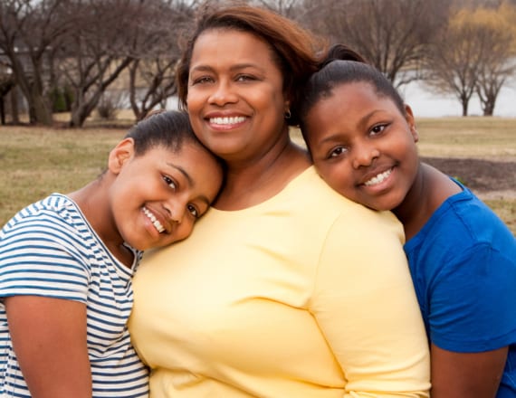 Mom in yellow shirt with her two young teenage kids in a park, all close together and smiling