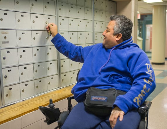 Middle-aged wheelchair user checking his mailbox in his apartment building