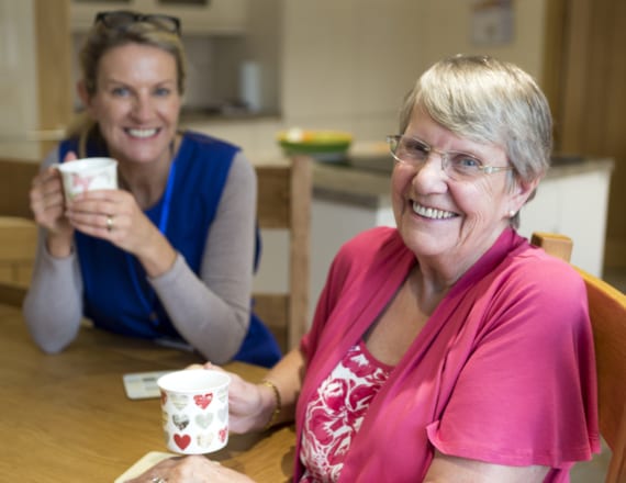 A social worker and an older woman sharing a friendly cup of tea in the woman's home
