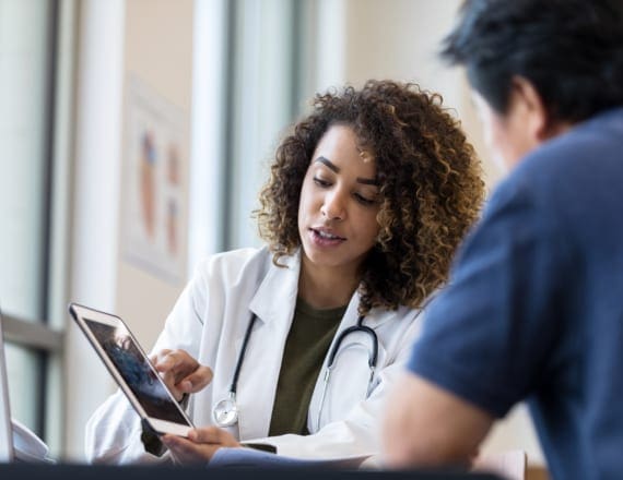 A doctor explains results to a patient, showing him something on a computer tablet