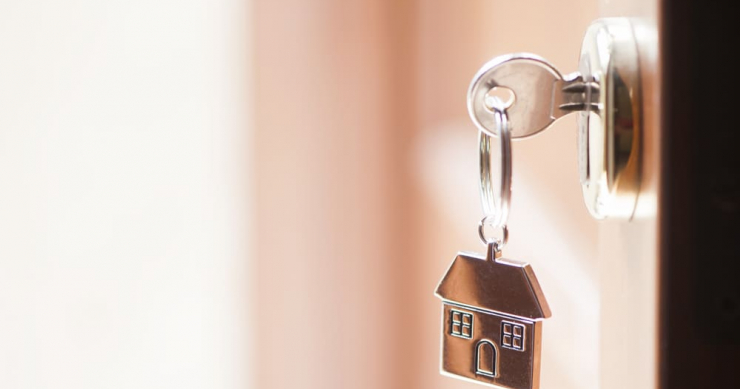 A key in the lock of a slightly open apartment door, with a house-shaped keychain hanging from the key