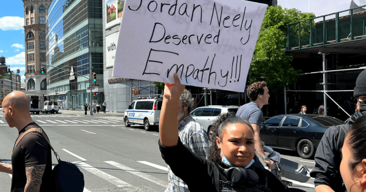 A participant in a "Justice for Jordan Neely" demonstration holds up a handwritten sign that reads "Jordan Neely Deserved Empathy!!!"